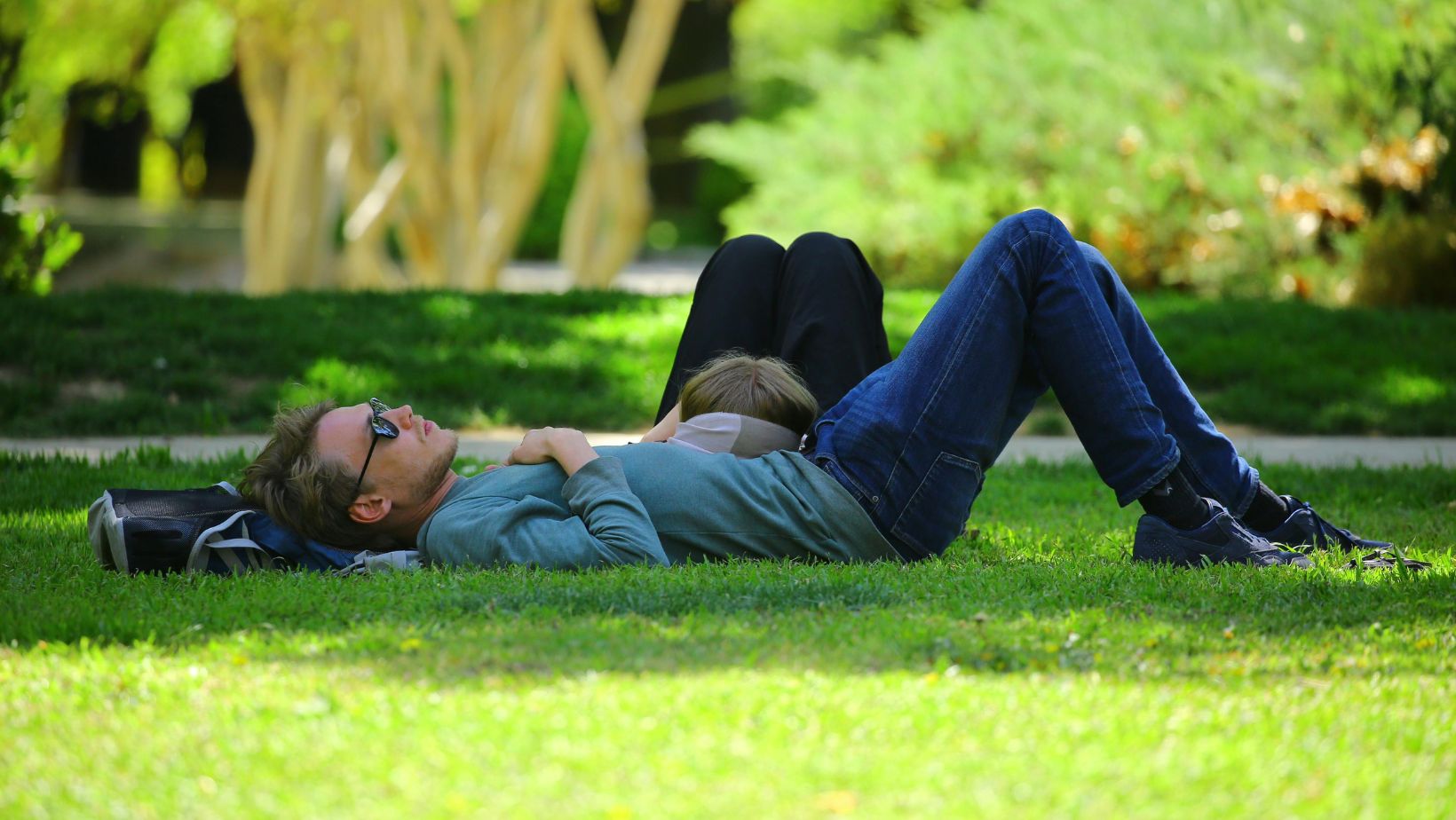 Two people lying together on the grass in a park.